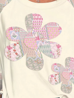 Cream long-sleeve shirt with large floral patchwork appliques in pink, green, and blue patterns.