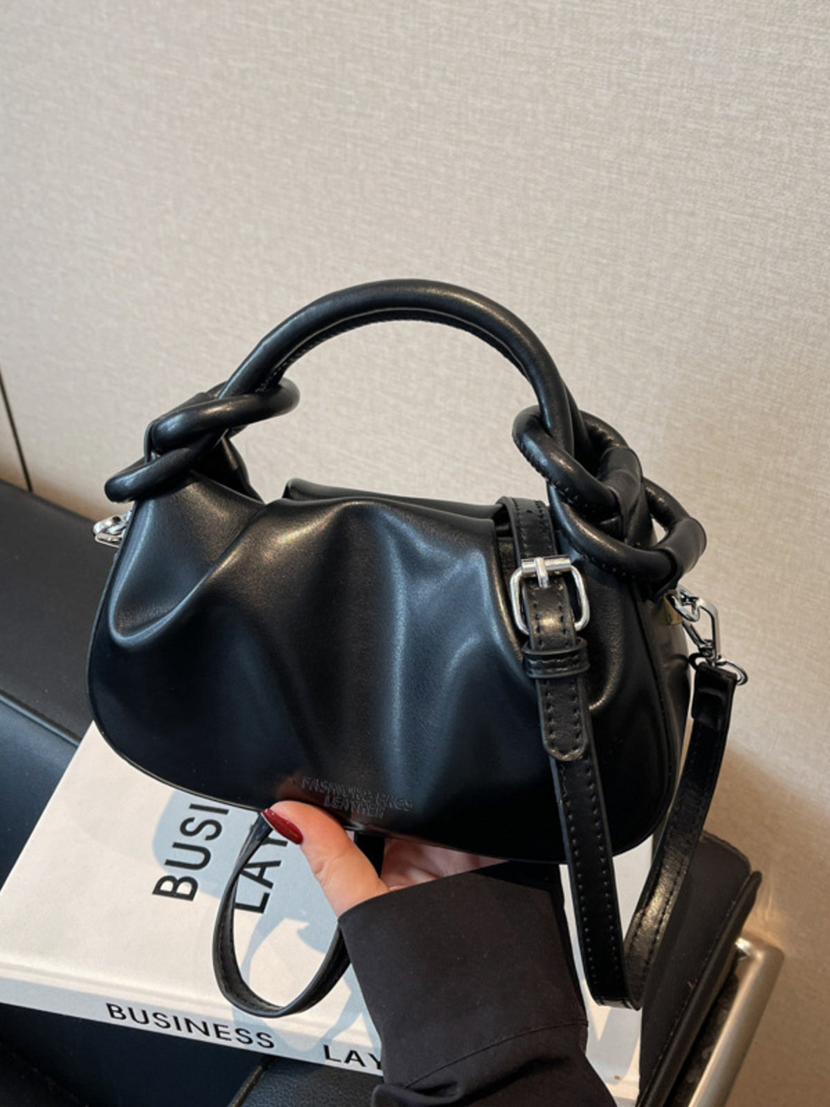 Black ruched crossbody bag with knot handle and adjustable strap.