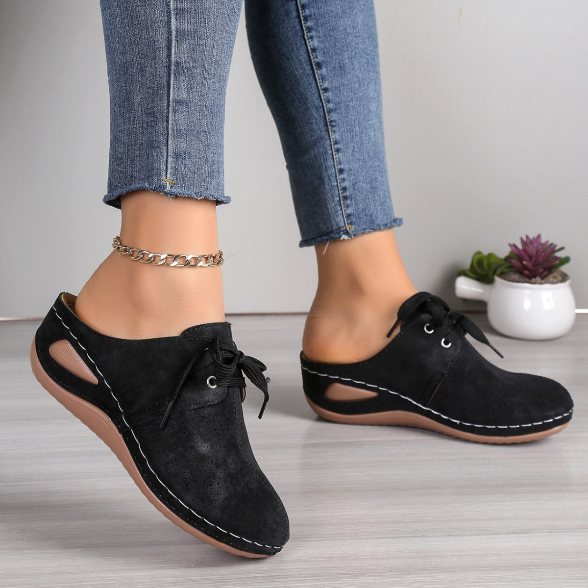 Black perforated lace-up slip-on mules with white stitching and cut-out sides.