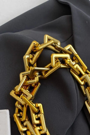 Quilted nylon tote bag detail with chunky gold chain handle on black fabric.