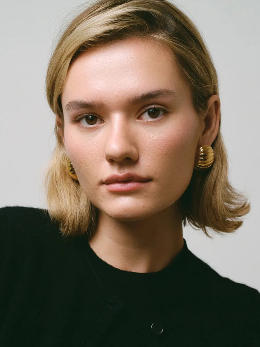 Gold dome earrings with ribbed texture, 18K gold-plated, worn by a woman.