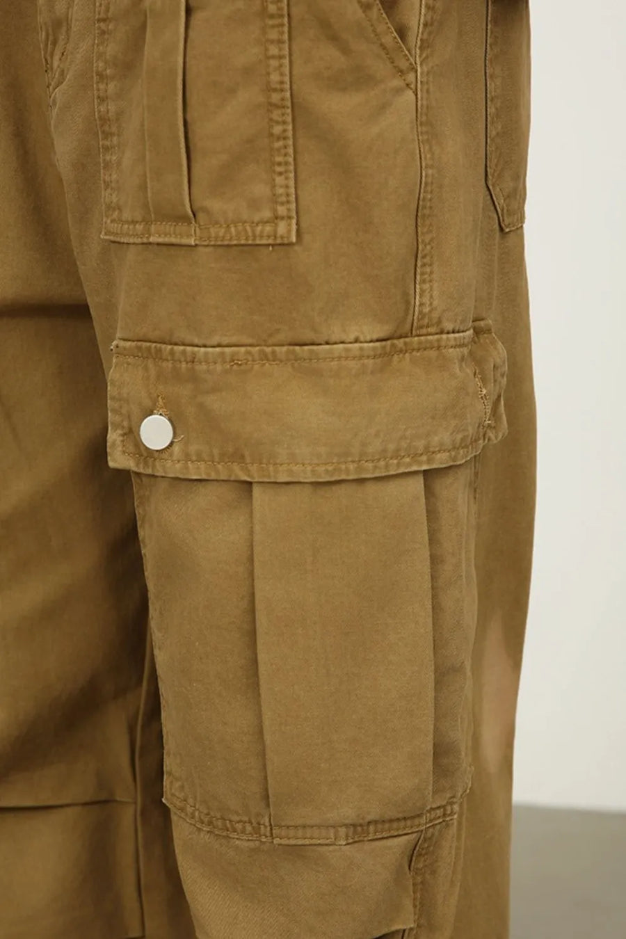 Khaki cargo pants with large pleated side pockets and button closures.
