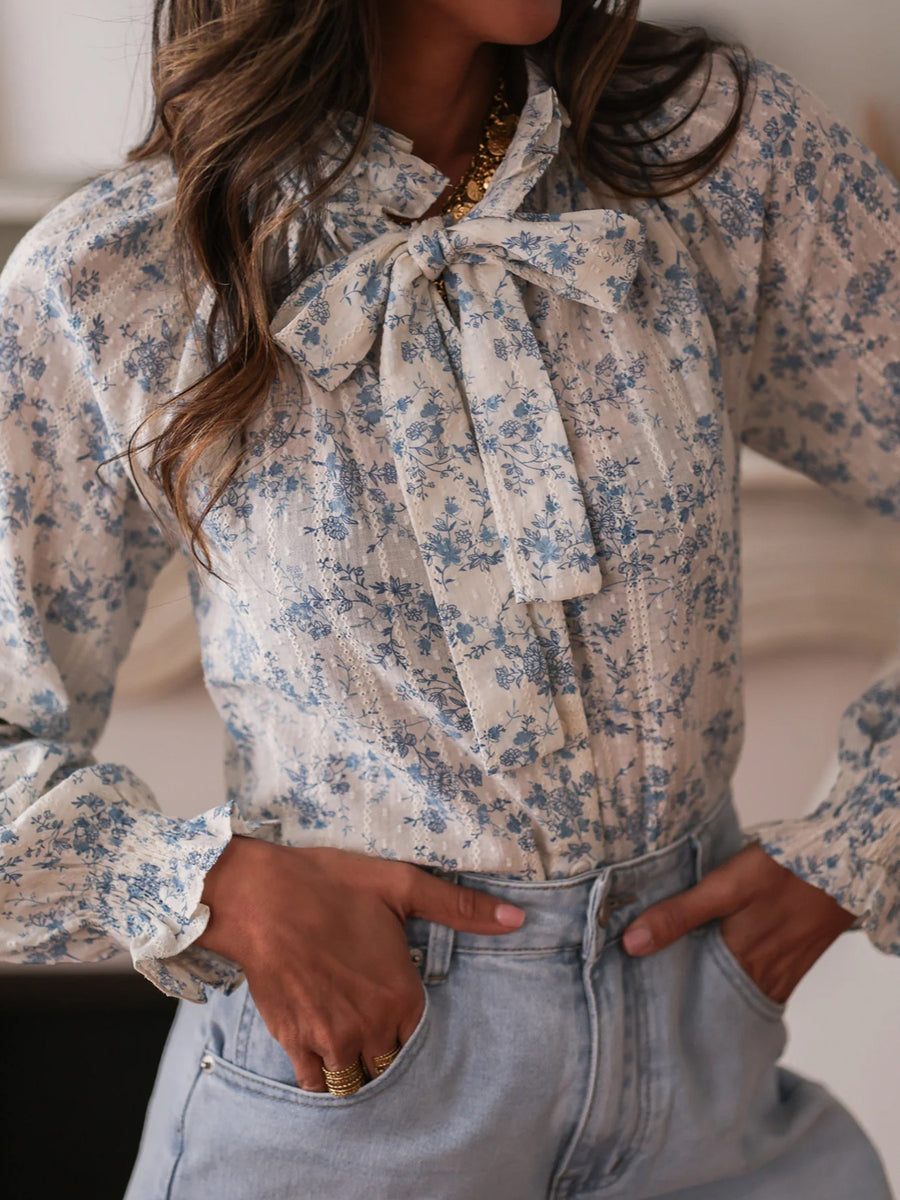 Floral tie neck long-sleeve blouse with blue floral print and ruffled cuffs.