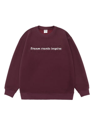 Oversized dark purple crew-neck sweatshirt with embossed text "Dream create inspire