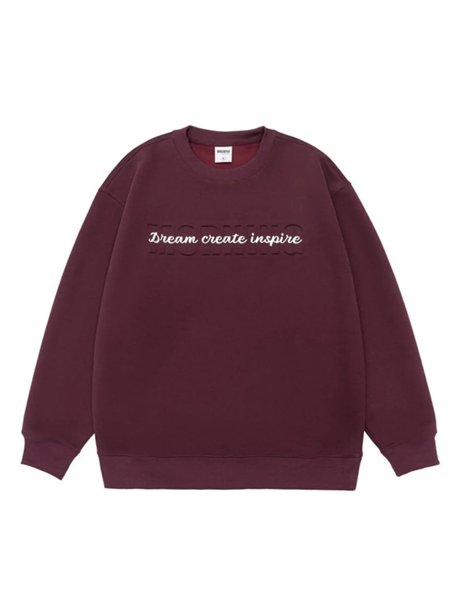 Oversized dark purple crew-neck sweatshirt with embossed text "Dream create inspire