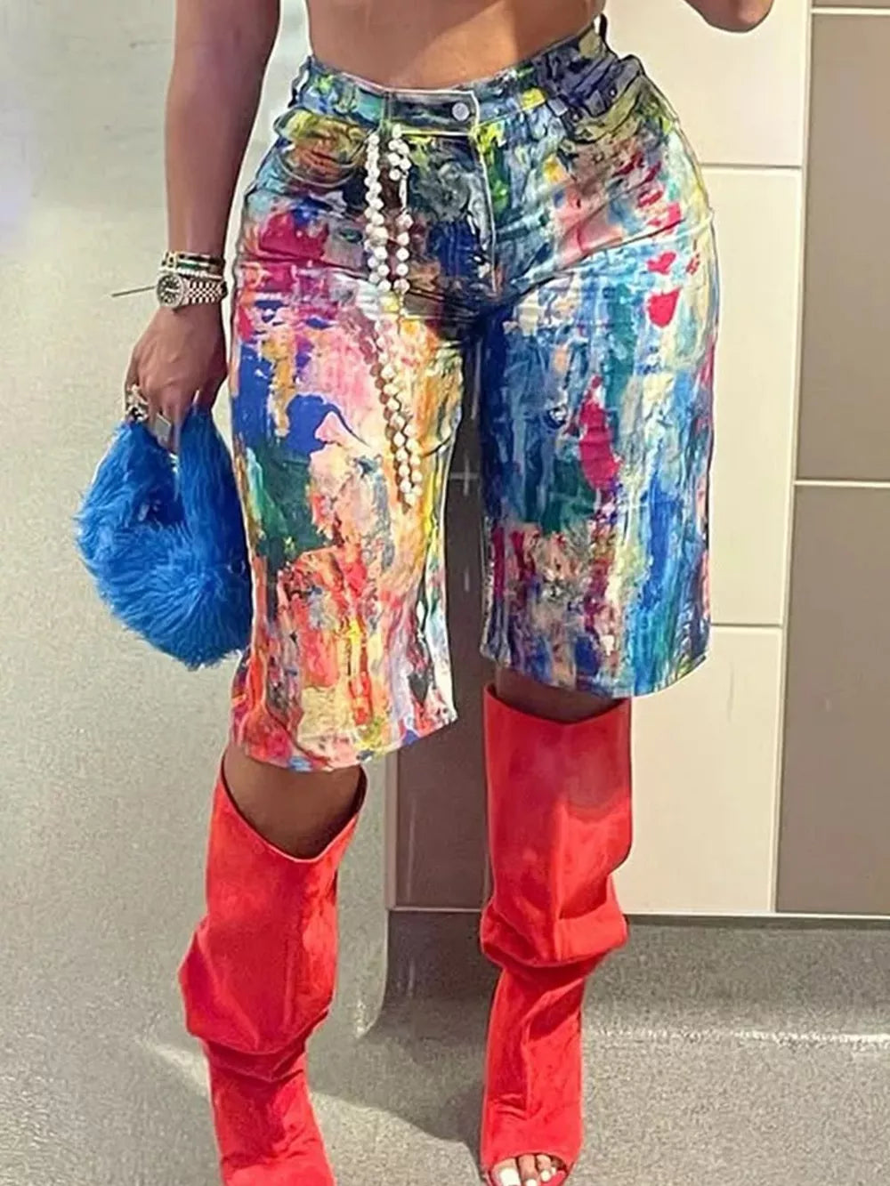 Denim shorts with abstract paint splatter pattern, pearl belt detail, styled with red slouch boots.