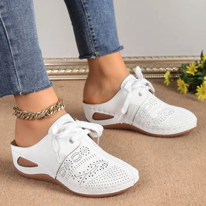 White perforated lace-up mule flats with cutout sides and tie detail.
