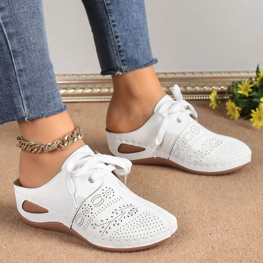 White perforated lace-up mule flats with cutout sides and tie detail.