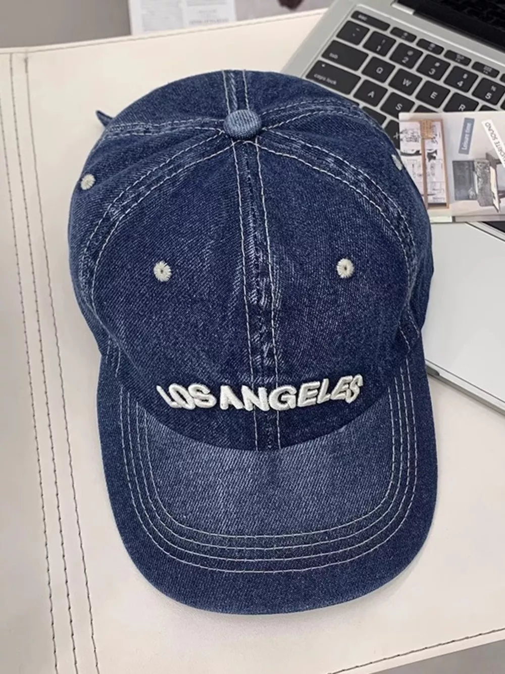 Dark blue denim baseball cap with white Los Angeles embroidery and contrast stitching.