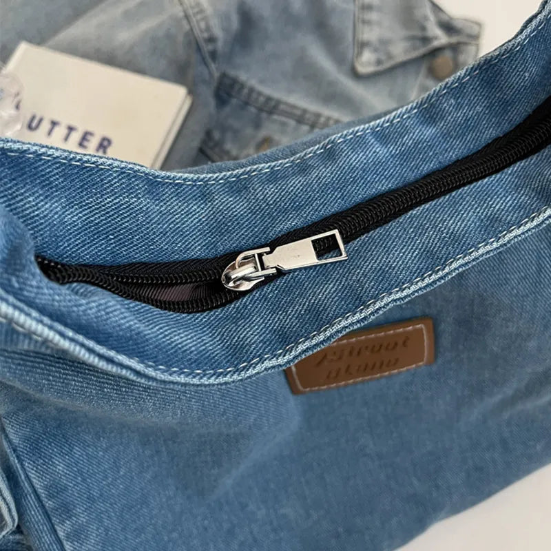 Light wash denim hobo bag with black zipper and leatherette patch detail.