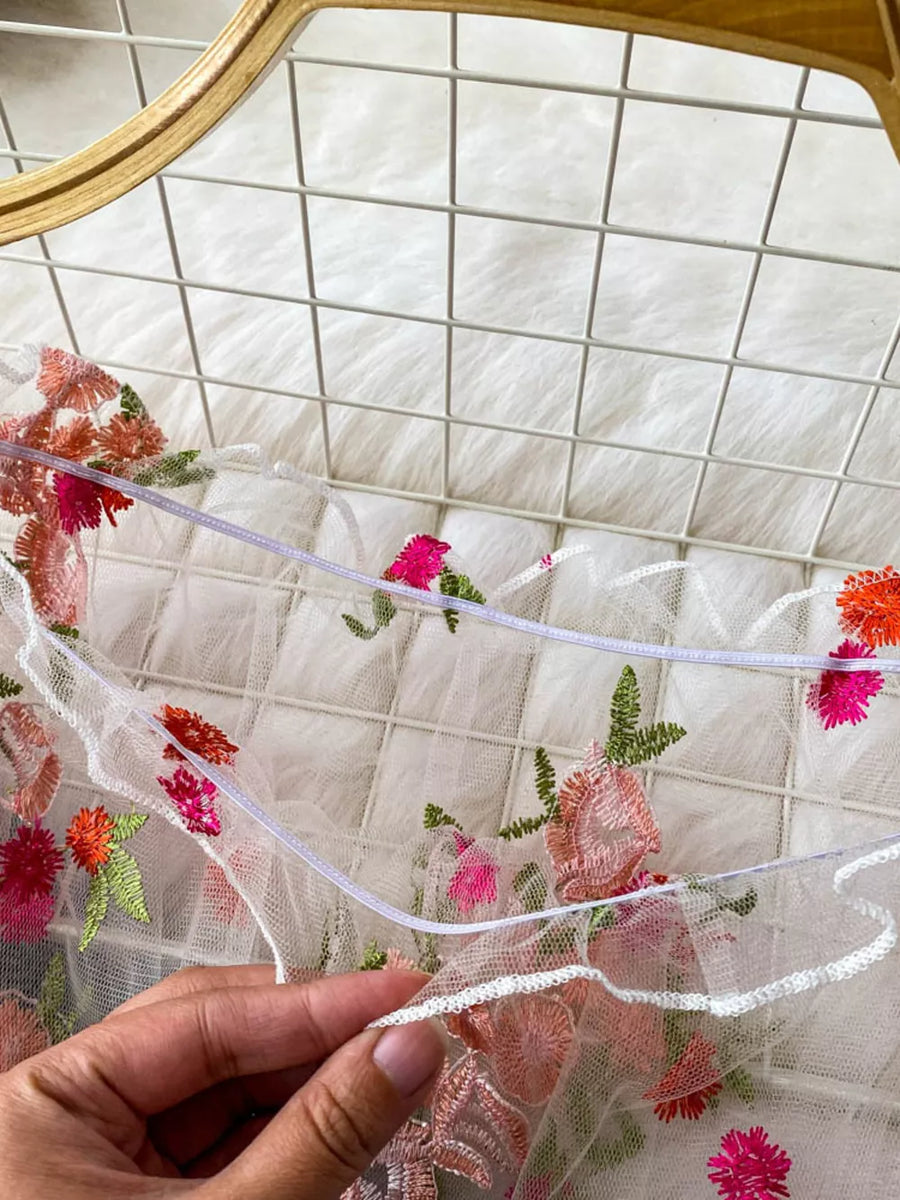 White off-shoulder t-shirt with colorful floral embroidery and sheer mesh fabric.