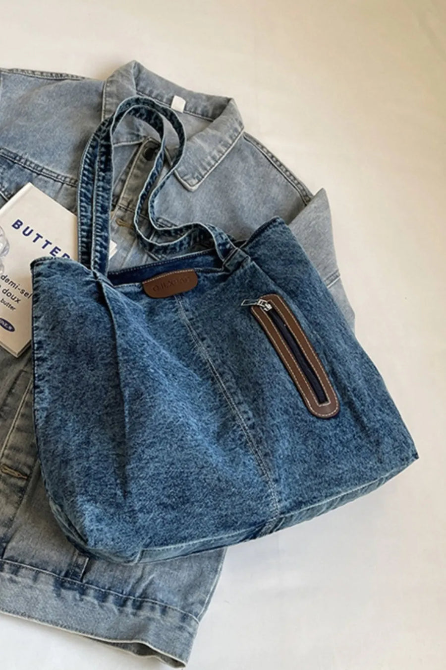 Denim tote bag with leather trim and zippered pocket, shown in medium blue wash.