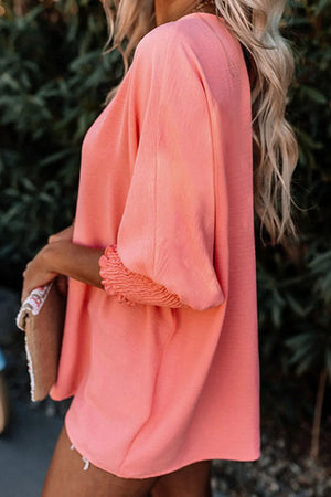 Coral blouson sleeve blouse with smocked cuffs and a textured fabric.