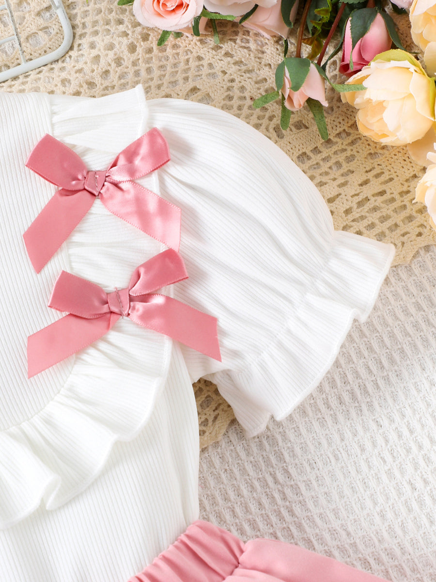 White ribbed toddler top with pink satin bows and ruffled sleeves.
