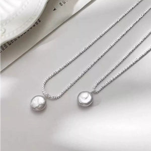 Elegant pearl pendant necklace with silver chain and textured finish.