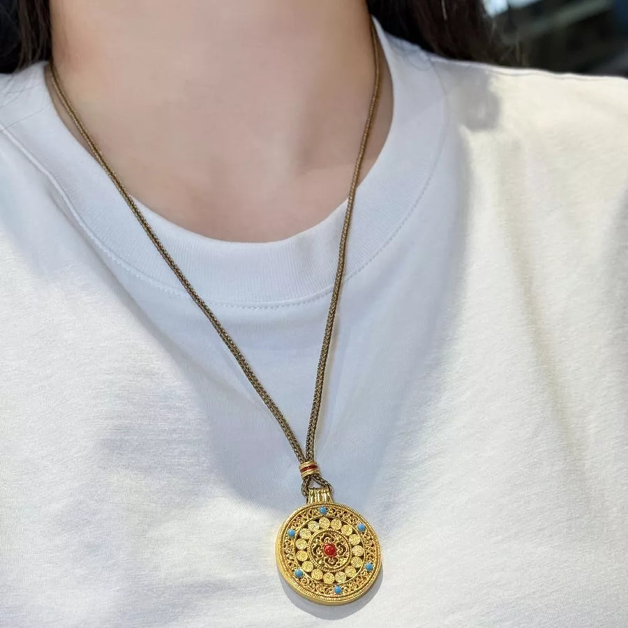 Gold-plated round pendant necklace with red and blue stones on a chain.