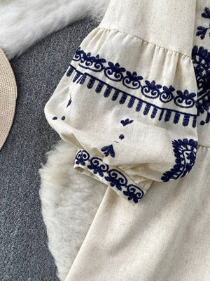 Cream tie-neck blouse with balloon sleeves and intricate navy embroidery detail.