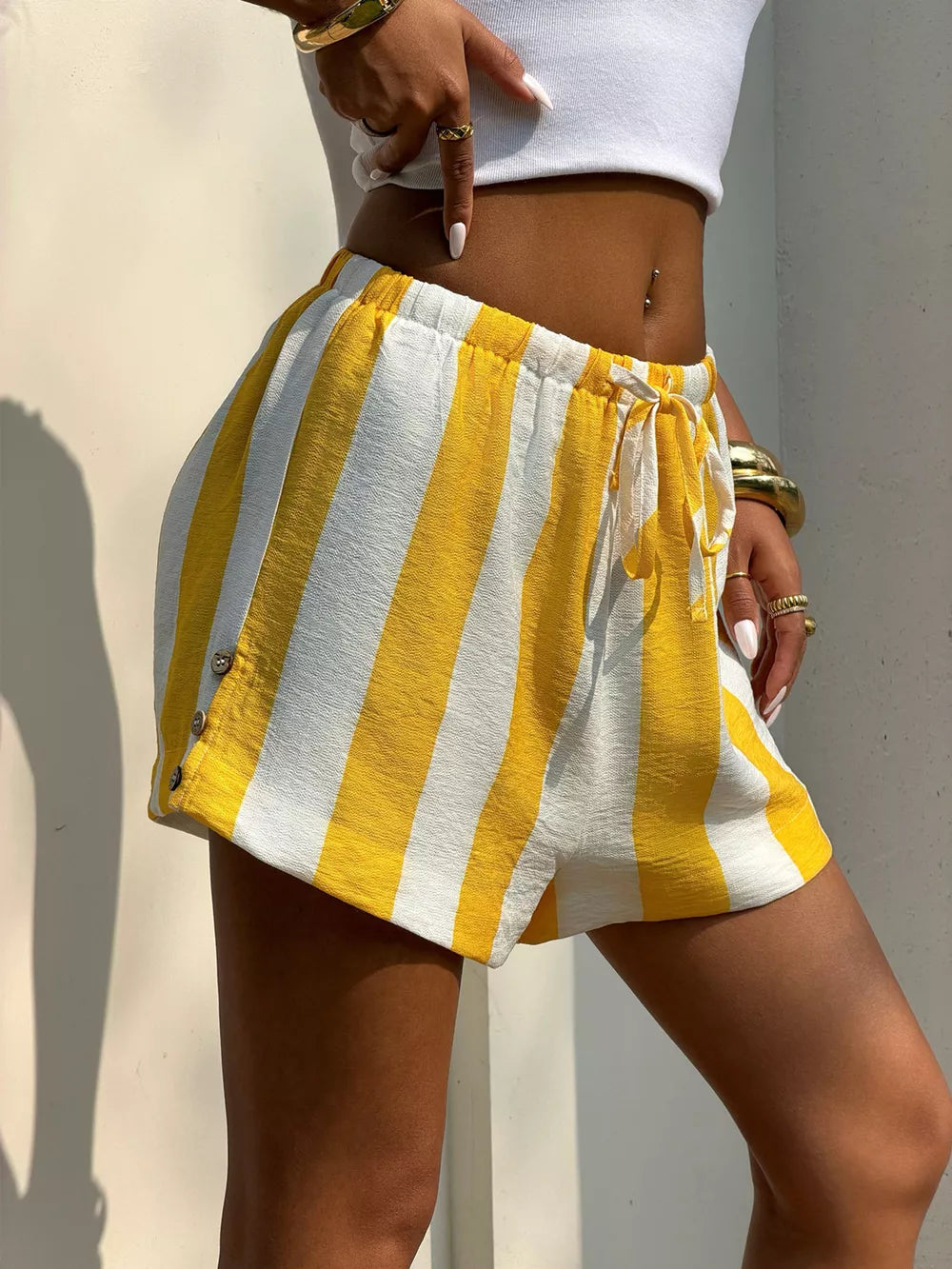 Yellow and white striped drawstring shorts with button detail at hem.