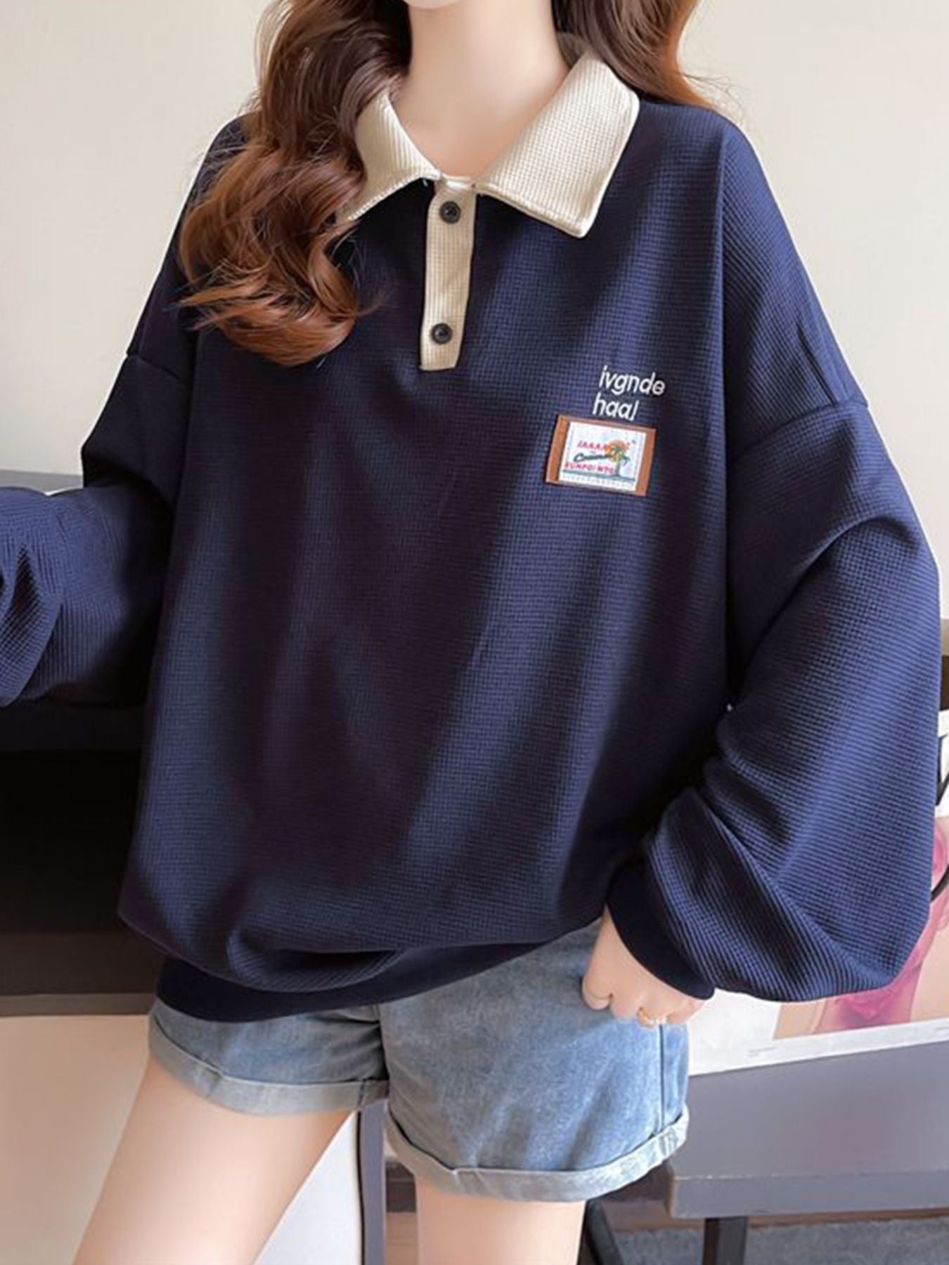 Navy waffle-knit polo sweatshirt with contrast collar and button placket, featuring a graphic patch.