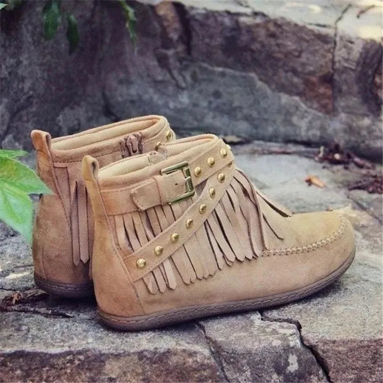 Beige suede ankle boots with fringe, studs, and buckle detail.