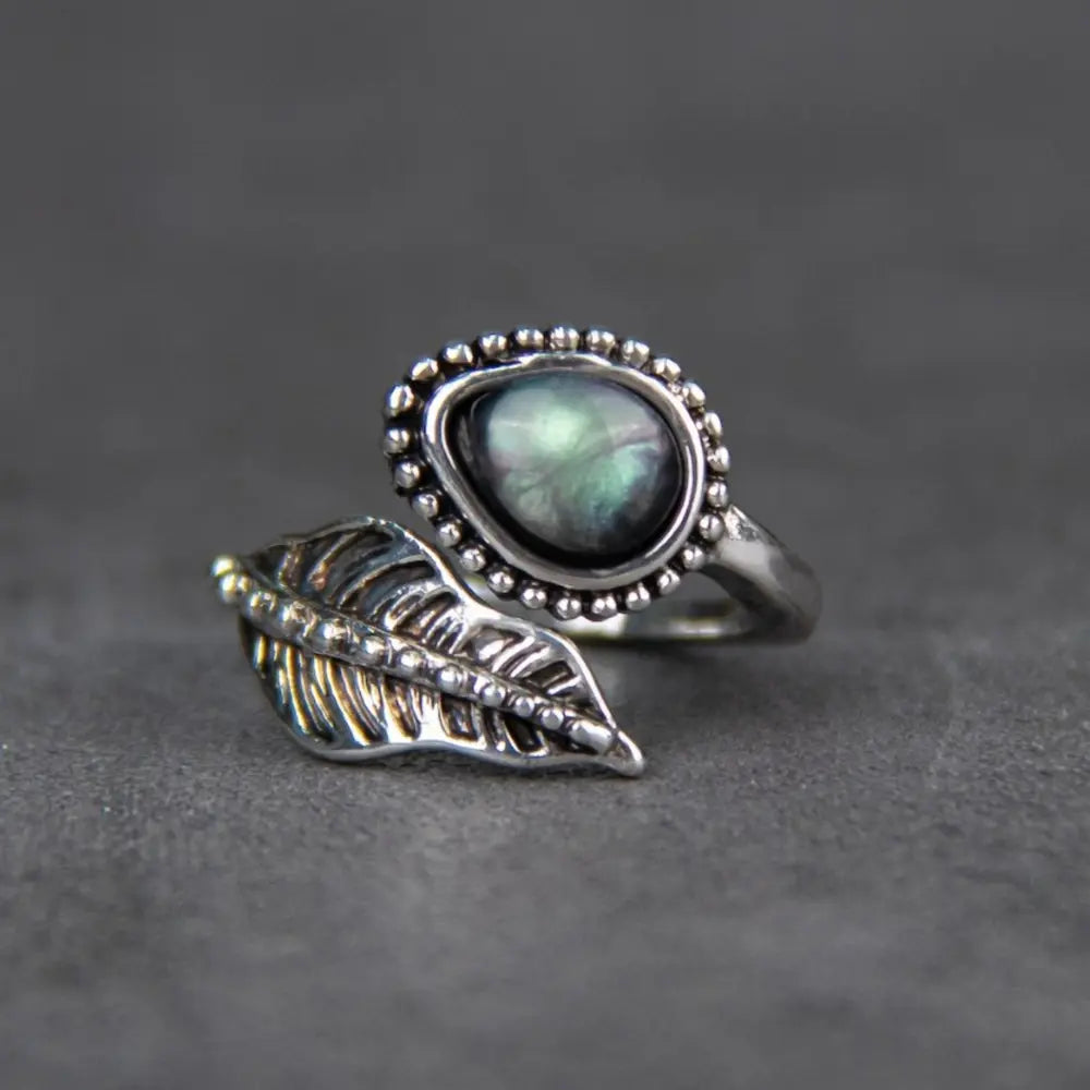 Silver bypass ring with a pearly oval stone and a detailed leaf design.
