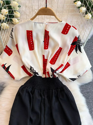White abstract print wide-leg romper with black smocked waist and short sleeves.