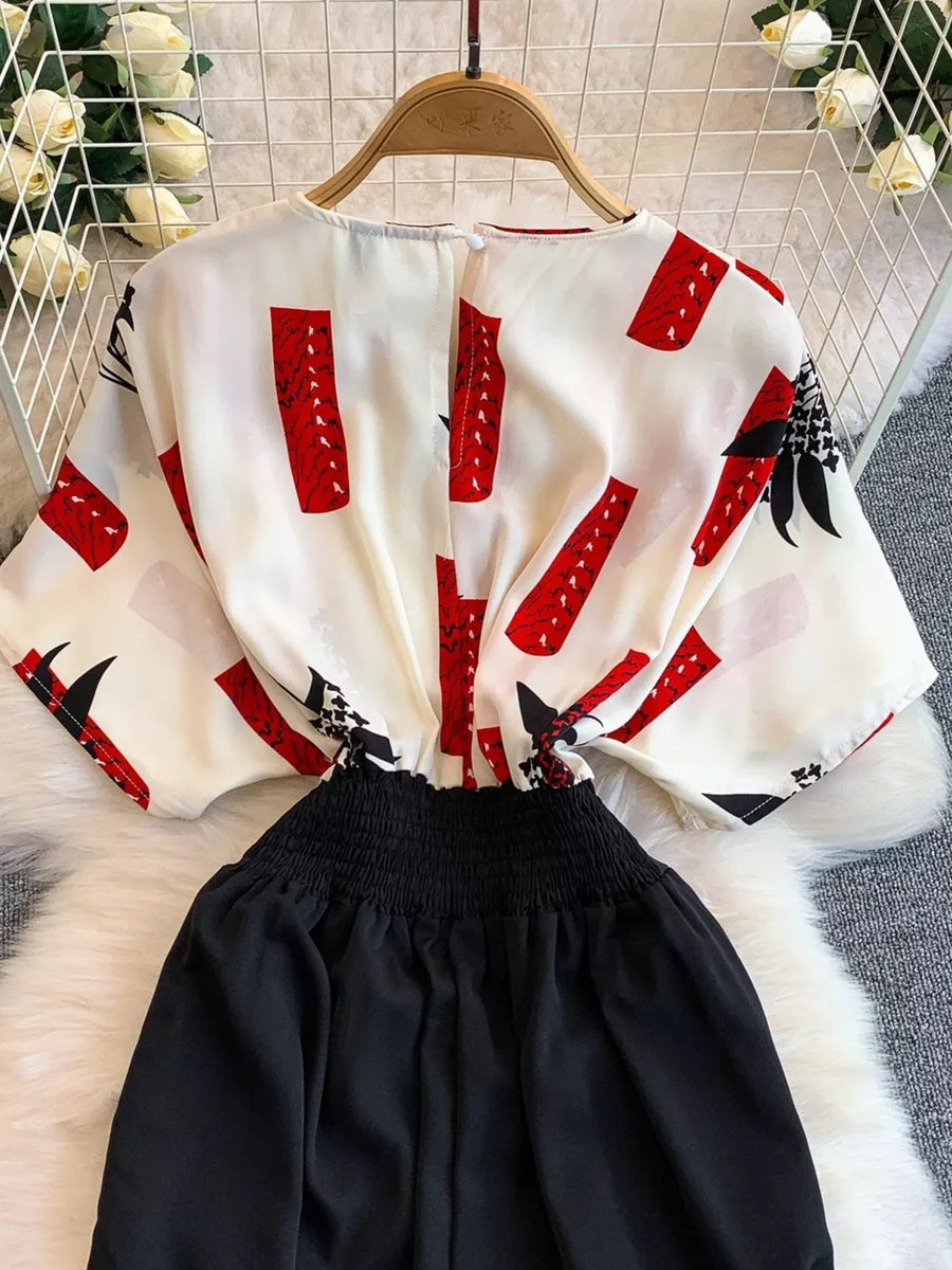 White abstract print wide-leg romper with black smocked waist and short sleeves.