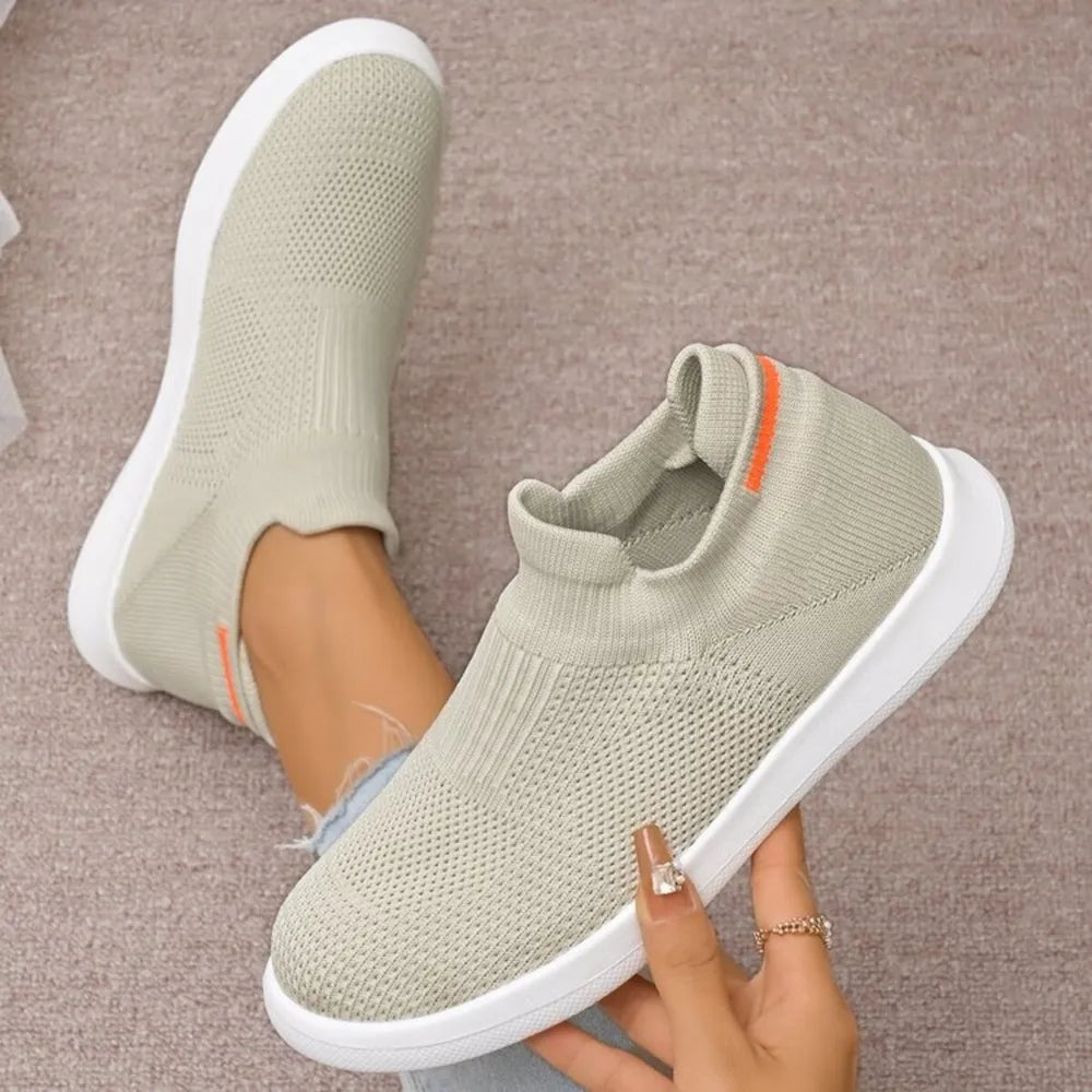 Light grey knit slip-on sneakers with white soles and orange heel detail.
