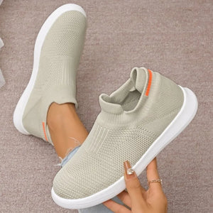 Light grey knit slip-on sneakers with white soles and orange heel detail.