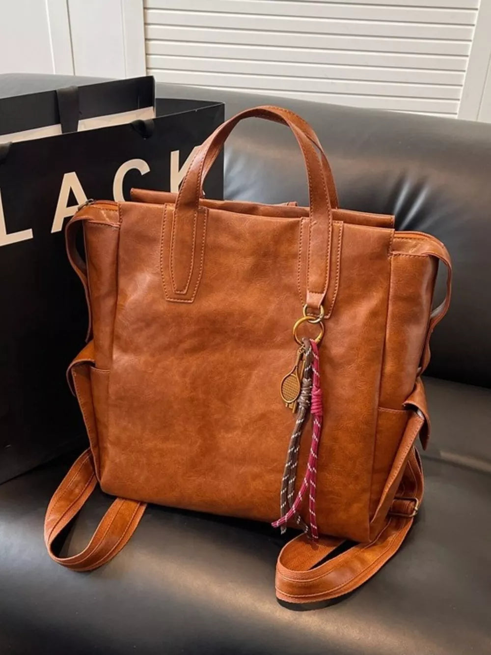 Convertible leather backpack in Terracotta with dual top handles and decorative keychain.