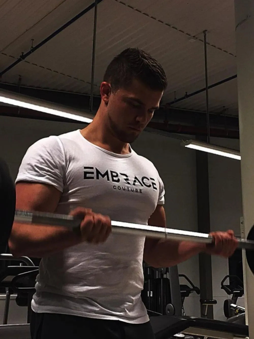 White t-shirt with black Embrace Couture logo, crew neck, short sleeves, casual fit.