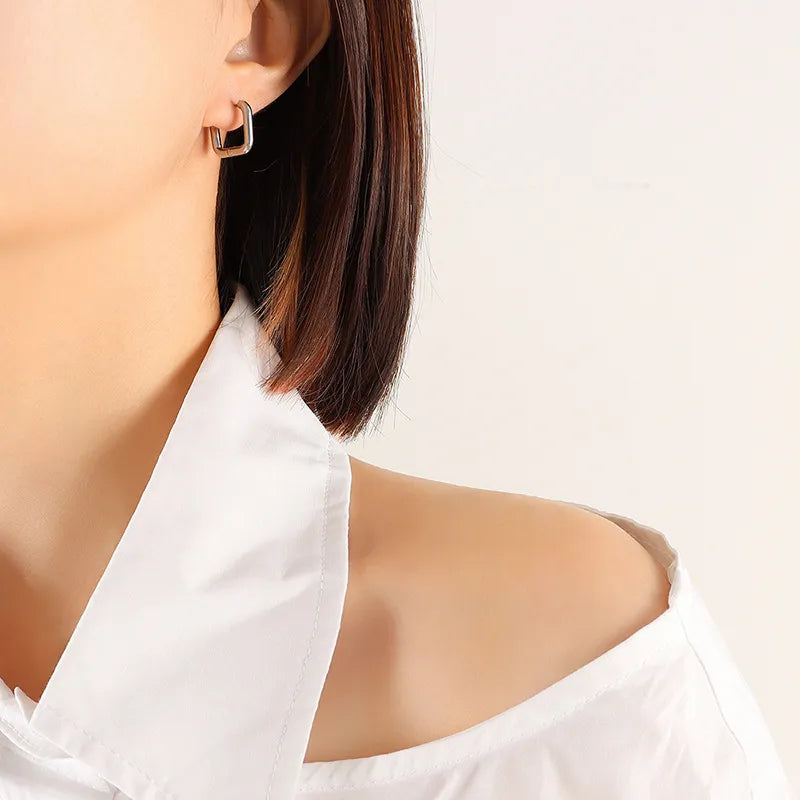 Silver Square geometric steel huggie earrings on ear, styled with a white off-shoulder shirt.