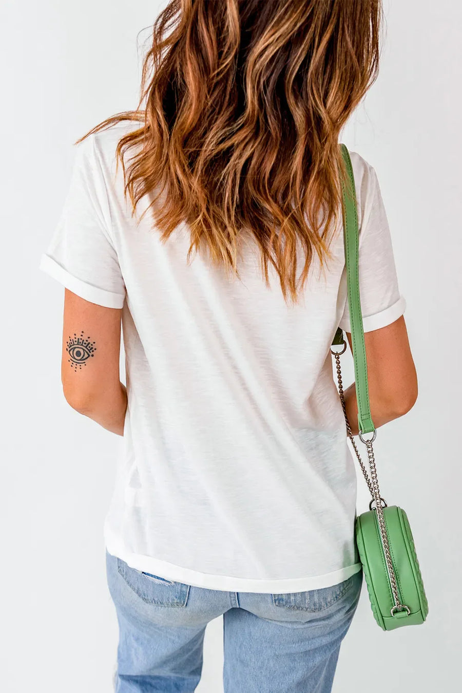 White graphic t-shirt with rolled sleeves and a subtle eye tattoo on the arm.