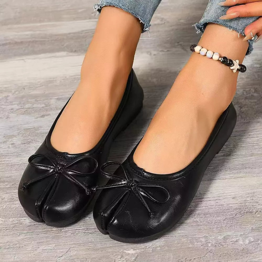 Black tabi slip-on flats with bow embellishments and split toe detail.