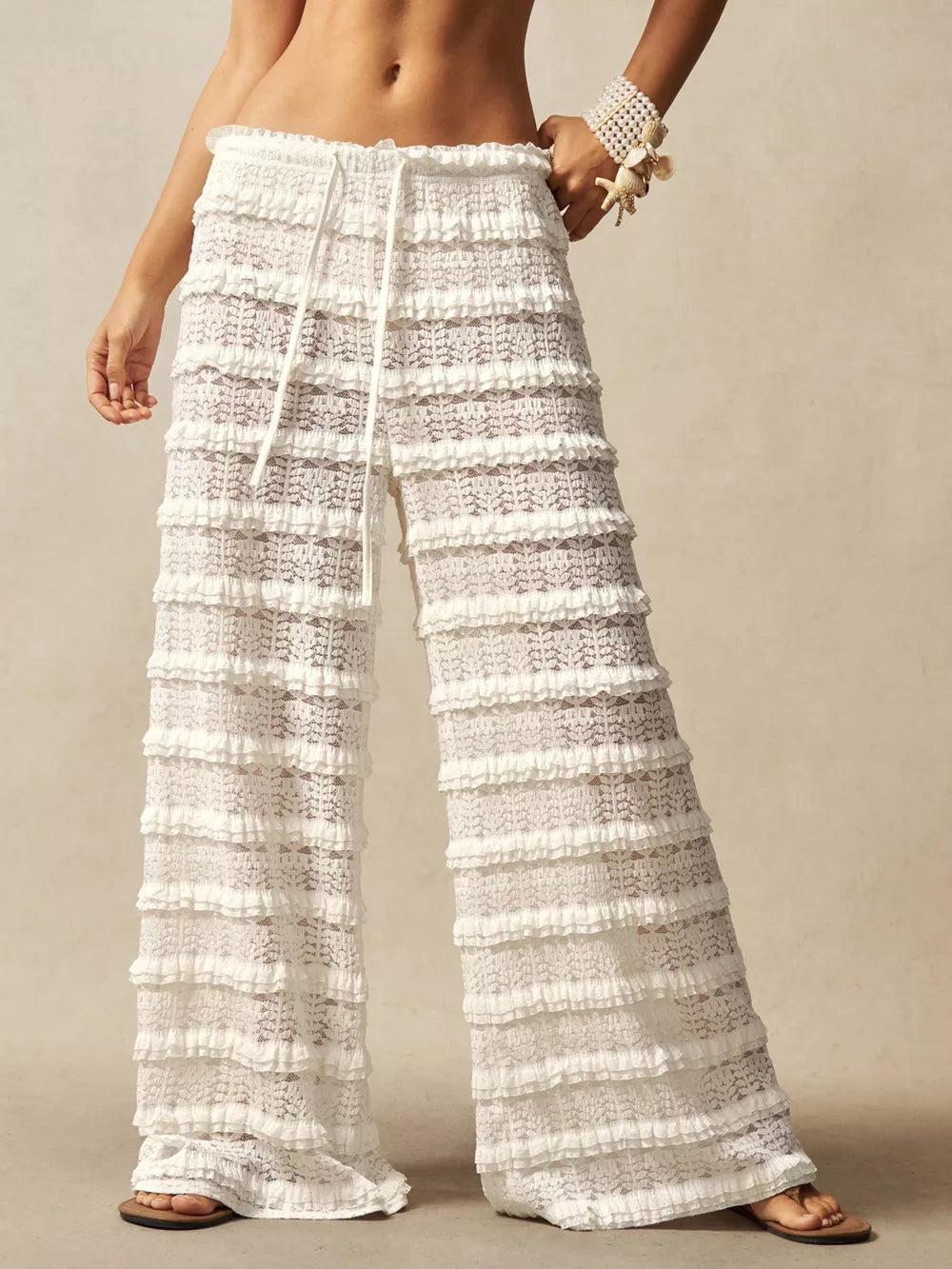 White lace wide-leg pants with tiered ruffles and a drawstring waist.