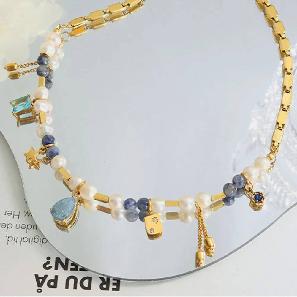 Gold celestial charm necklace with pearls, beads, and star, gem, and cube charms.