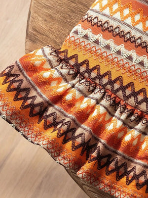 Baby dress with orange, white, and brown zigzag pattern and ruffled hem detail.