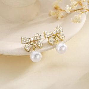 Gold bowknot pearl drop earrings with 18K gold plating and pearl accents.