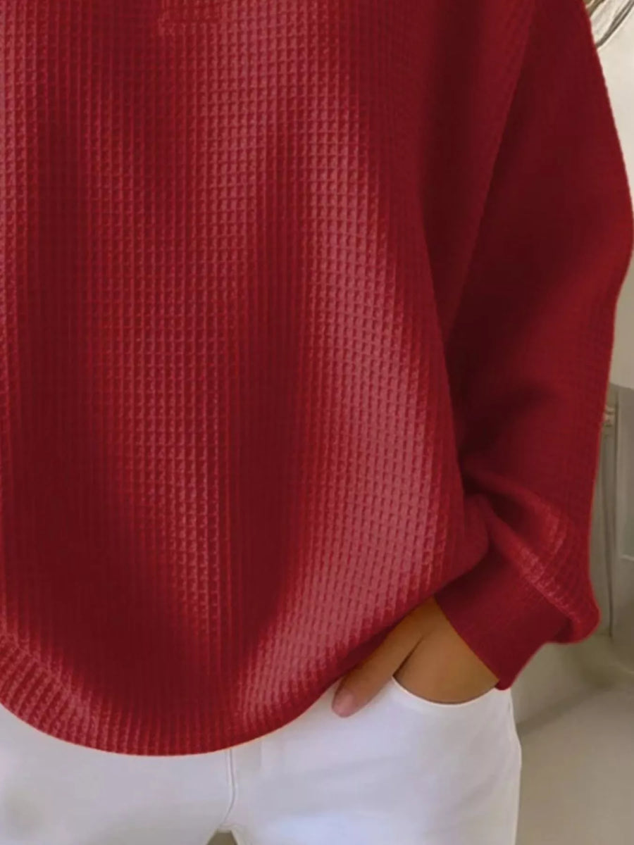 Red waffle knit top with button detail and long sleeves, paired with white pants.