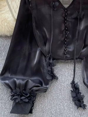 Black button-down shirt with delicate floral appliqué embellishments on the sleeves and neckline.