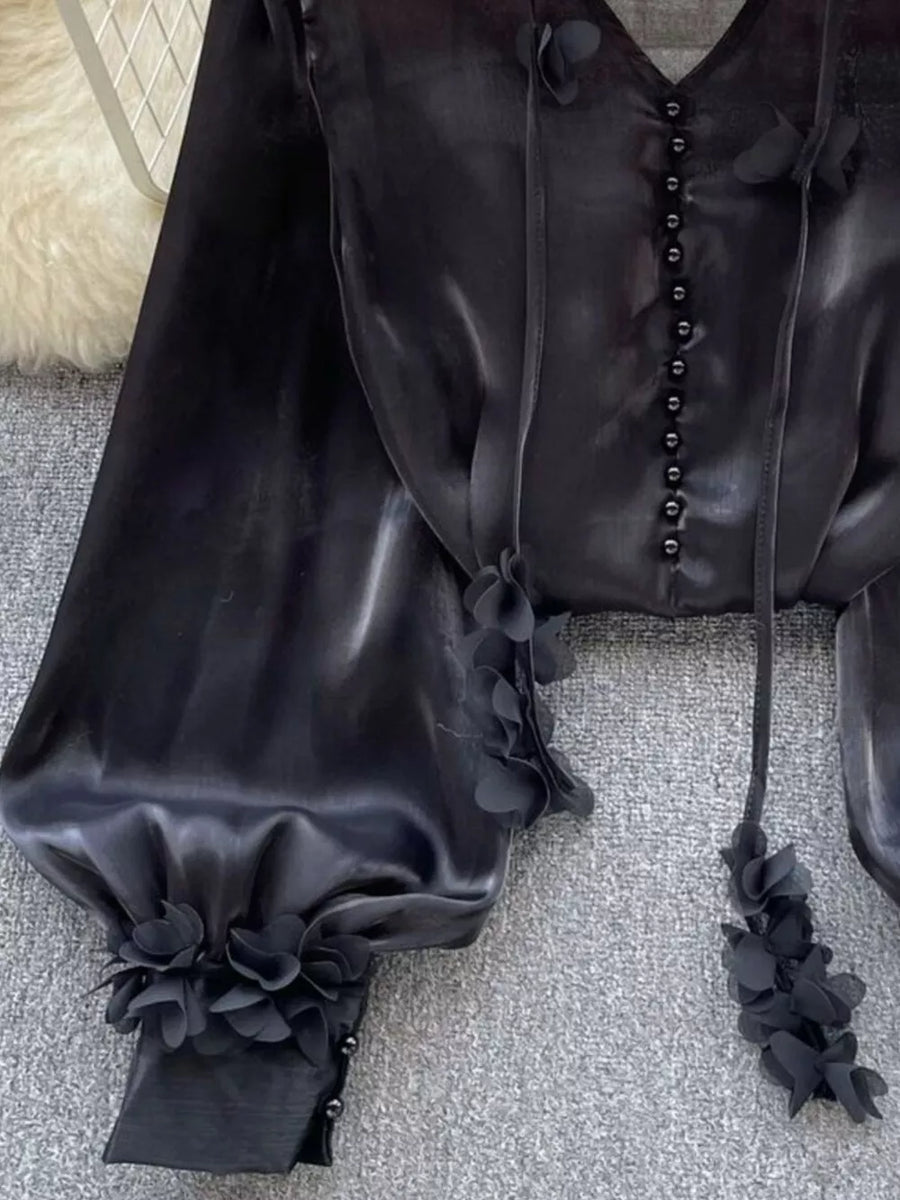 Black button-down shirt with delicate floral appliqué embellishments on the sleeves and neckline.