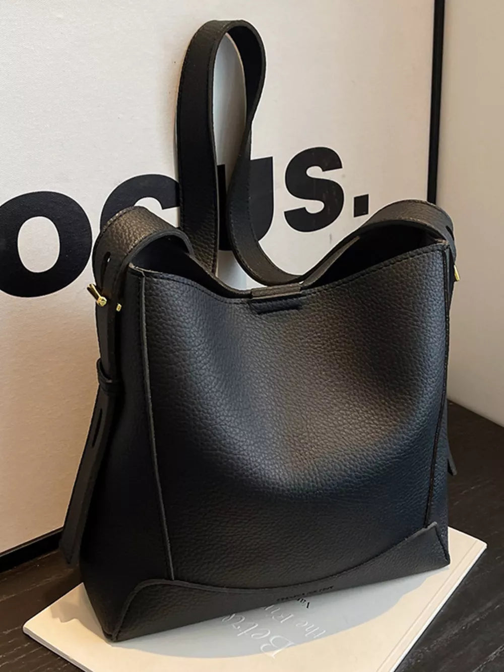 Black pebbled leather crossbody bag with adjustable strap and gold hardware detail.