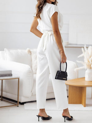 White draped wrap-front wide-leg jumpsuit with a tie waist, styled with black heels and a mini bag.