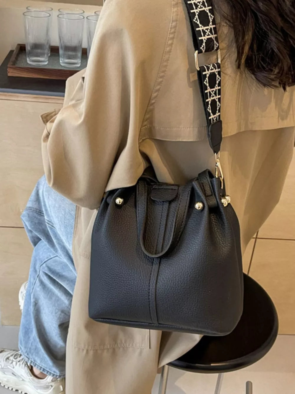 Textured black crossbody bag with unique patterned strap and drawstring closure.
