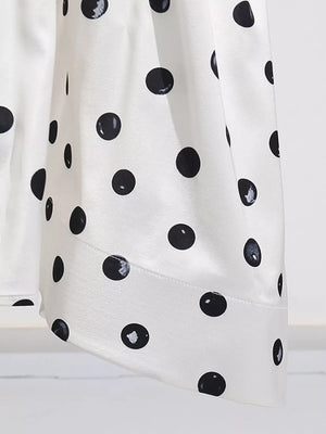 White satin dress with black polka dots, featuring a flowing silhouette.