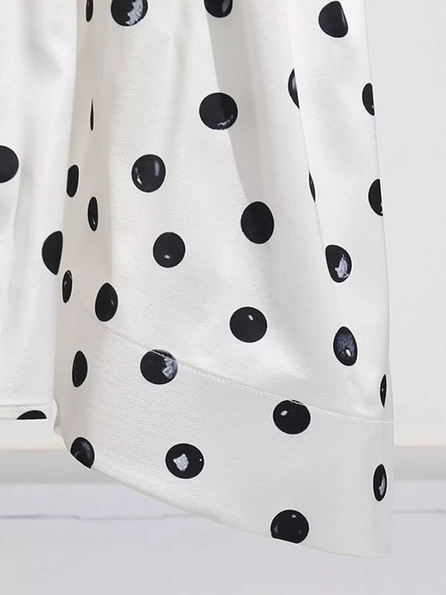 White satin dress with black polka dots, featuring a flowing silhouette.