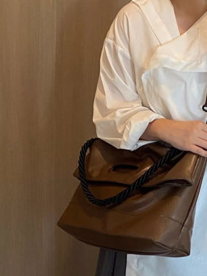 Oversized brown PU leather tote bag with twisted black strap and cutout handle detail.