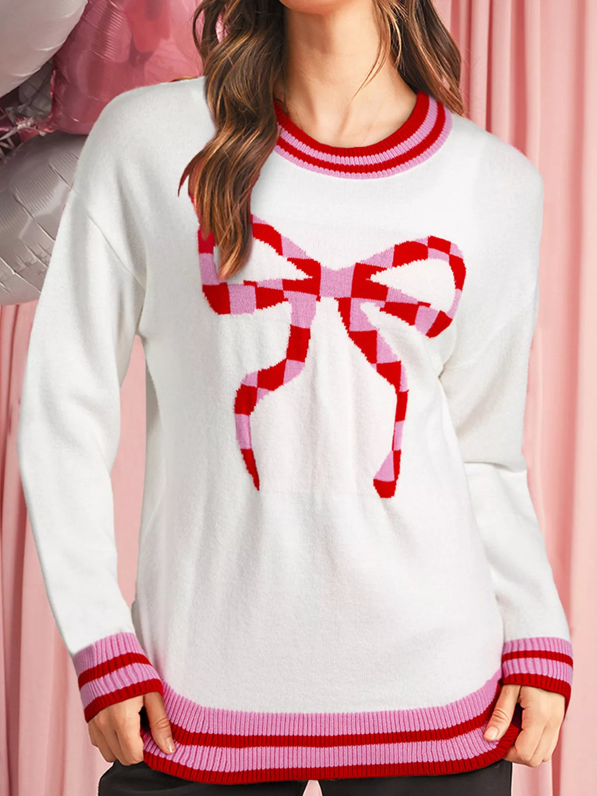 White round-neck sweater with a red and pink checkered bow graphic and striped cuffs and hem.