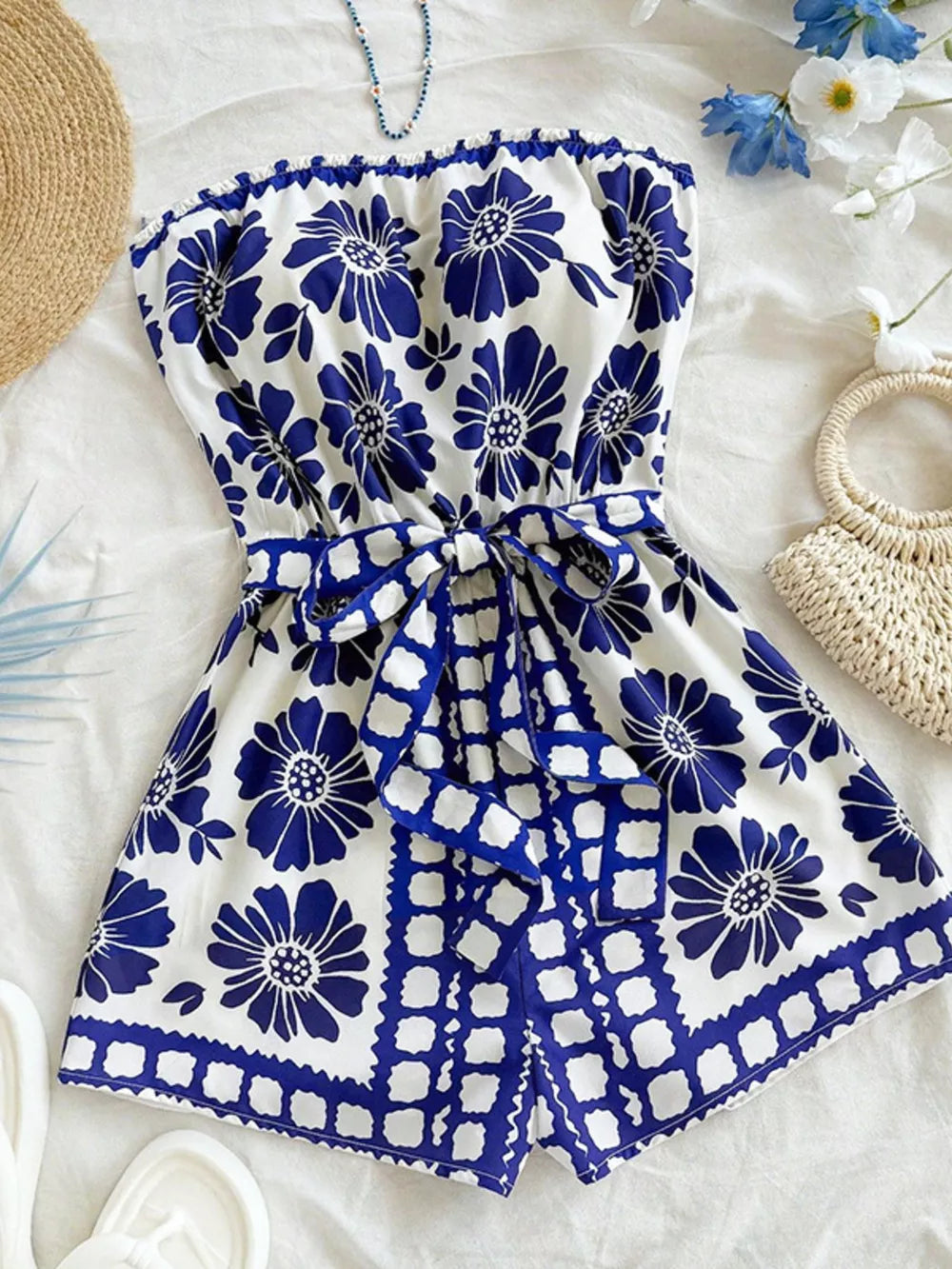 Blue floral tie-waist strapless romper with a ruffled hem and tie detail.