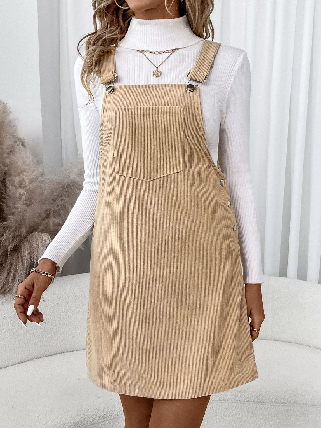 Tan corduroy overall dress with a front pocket and button side details.